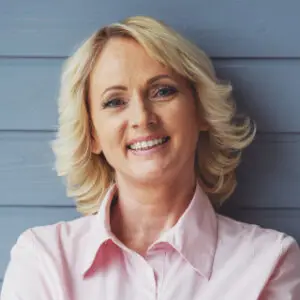 Beautiful middle-aged woman smiling in pink shirt and blue background.