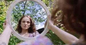 Young woman looking at herself in a mirror outside.
