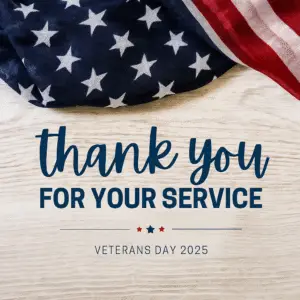 An American flag draped across the top of a light wooden background with navy text reading ‘thank you FOR YOUR SERVICE’ and smaller text below that says ‘Veterans Day 2025,’ accented by small red and blue stars.