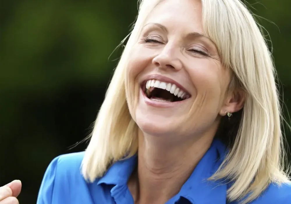 Blond woman with raised fists looking happy from meeting her hearing aid specialist.